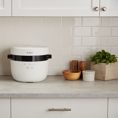 Weißer Instant Pot auf einer Küchenarbeitsplatte mit Küchenutensilien und Pflanzen.