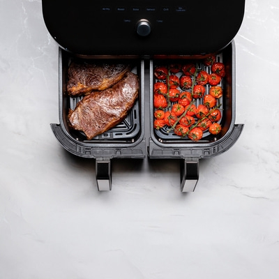 Luftfritteuse mit Steak und Tomaten auf weißem Marmor