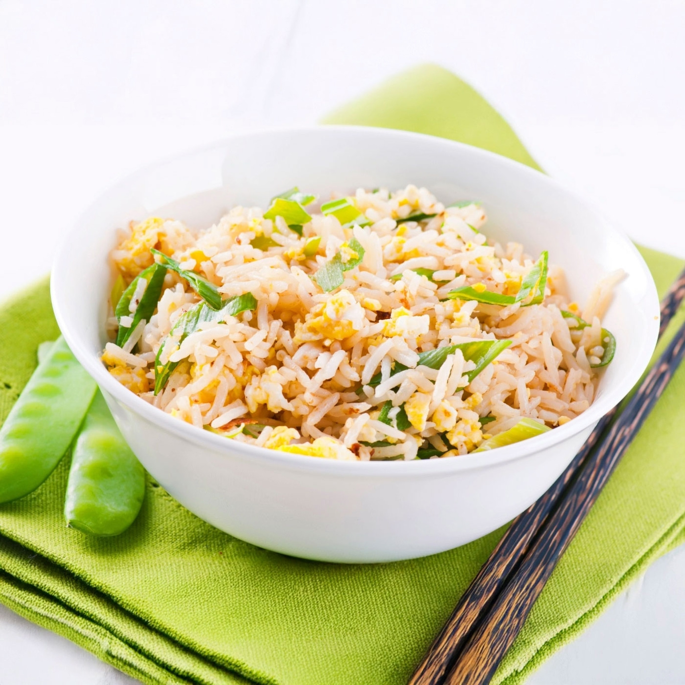 Schüssel mit gebratenem Reis, Stäbchen und Erbsen auf grünem Tuch