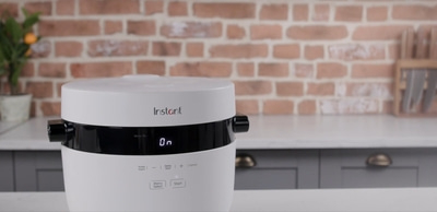 Instant Reiskocher, weiß, mit Bedienfeld und Ziegelwand im Hintergrund