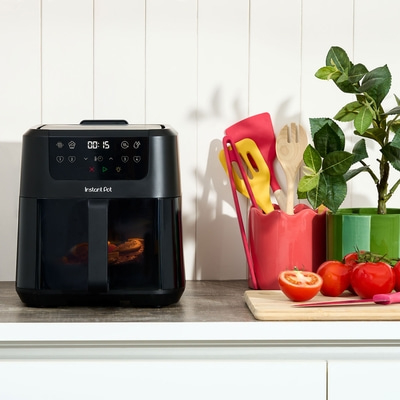 Schwarze Heißluftfritteuse mit Gemüse und Küchenutensilien auf einer Arbeitsplatte