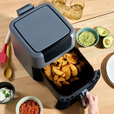 Luftfritteuse mit Pommes, Avocado, Dips und Getränken auf Holzoberfläche