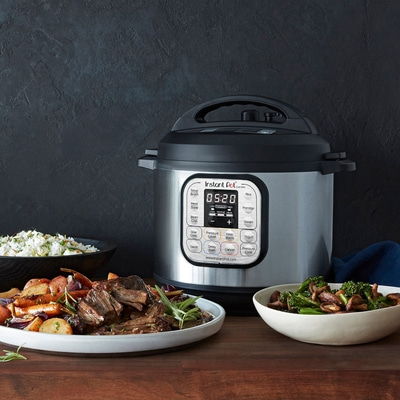 Instant Pot mit Essen, Gemüse und Fleisch auf einem Holztisch vor dunklem Hintergrund.