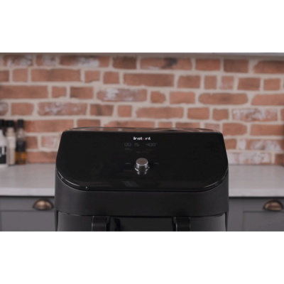 Schwarze Fritteuse mit Bedienfeld und Ziegelwand im Hintergrund. Instant-Marke.