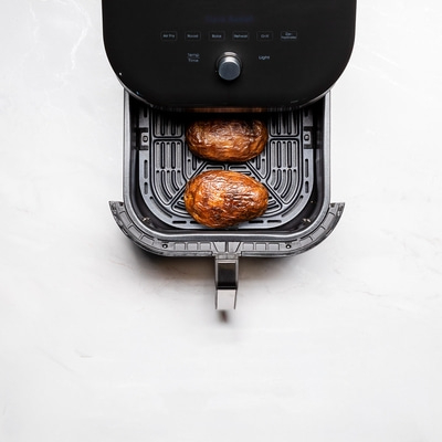 Luftfritteuse mit zwei Kartoffeln auf weißem Marmortisch