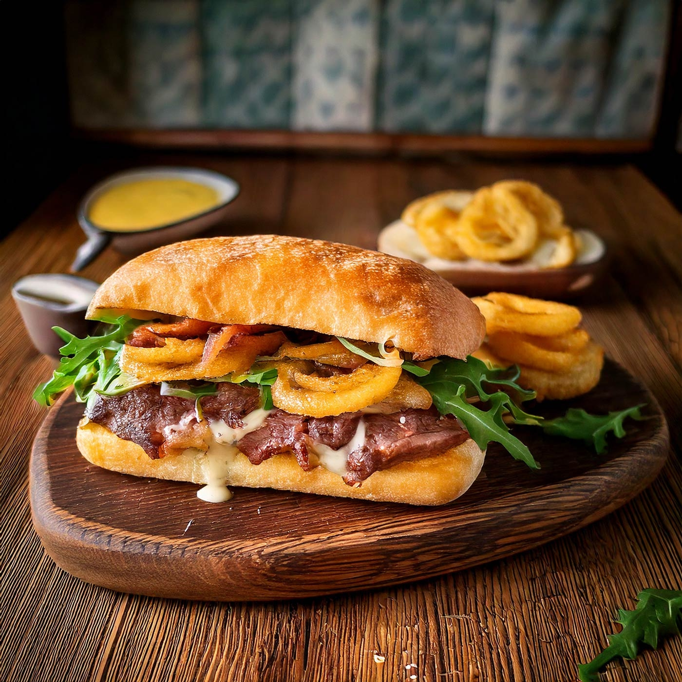 Ein köstliches Sandwich mit Zwiebelringen und Soße auf einem Holzbrett.