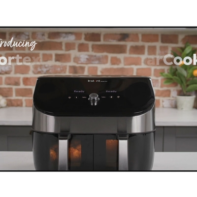 Schwarze Fritteuse mit zwei Fächern, bereit zum Kochen, mit Backsteinmauer im Hintergrund.