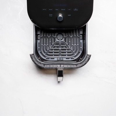 Schwarze Fritteuse mit geöffnetem Korb auf weißem Marmor