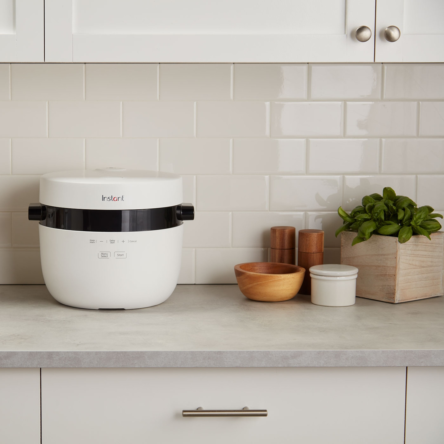 Weißer Instant Pot auf einer Küchenarbeitsplatte mit Küchenutensilien und Pflanzen.