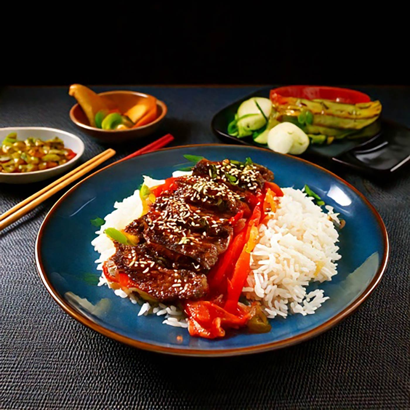 Asiatisches Gericht mit Reis, Fleisch und Gemüse auf einem blauen Teller