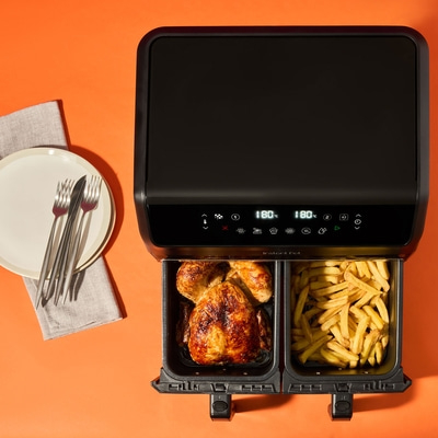 Frittiergerät mit Hähnchen und Pommes auf orangefarbenem Hintergrund