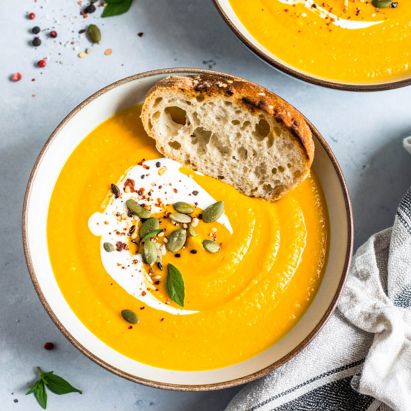 Kürbissuppe mit Brot, Sahne, Samen und Gewürzen in einer Schüssel auf grauem Hintergrund
